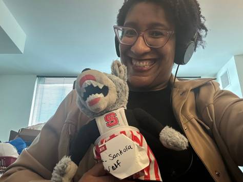 Kristen smiling holding a doll version of NC State University's Mrs. Wuf Mascot she's renamed Mx. Sanfoka Wuf