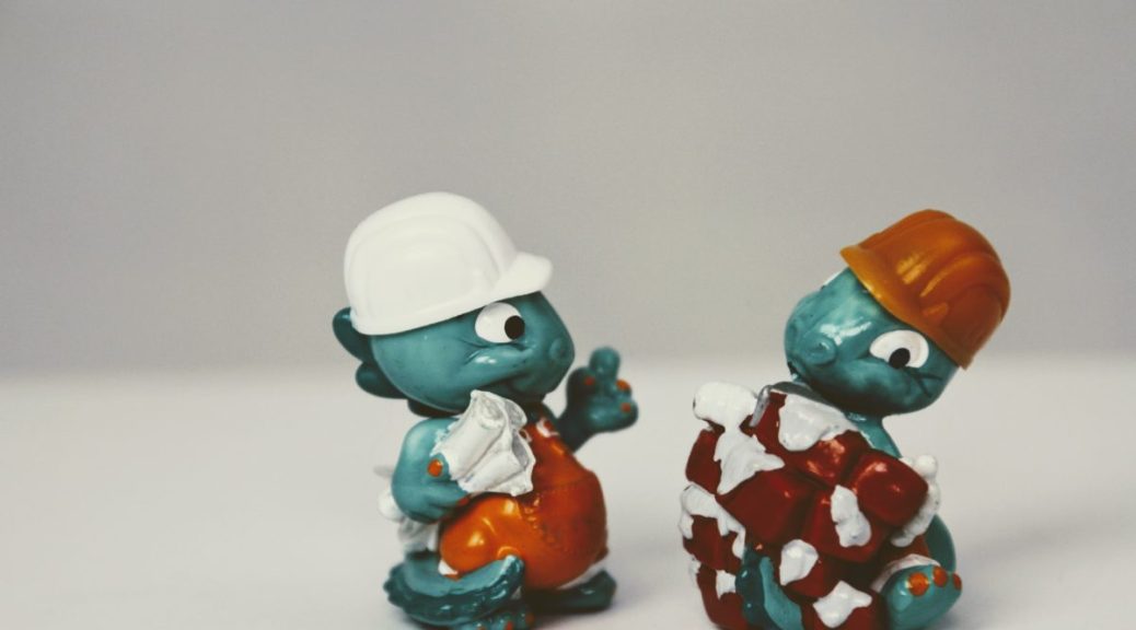 Two green toy clay dinosaurs in construction hats hang out behind a grey background