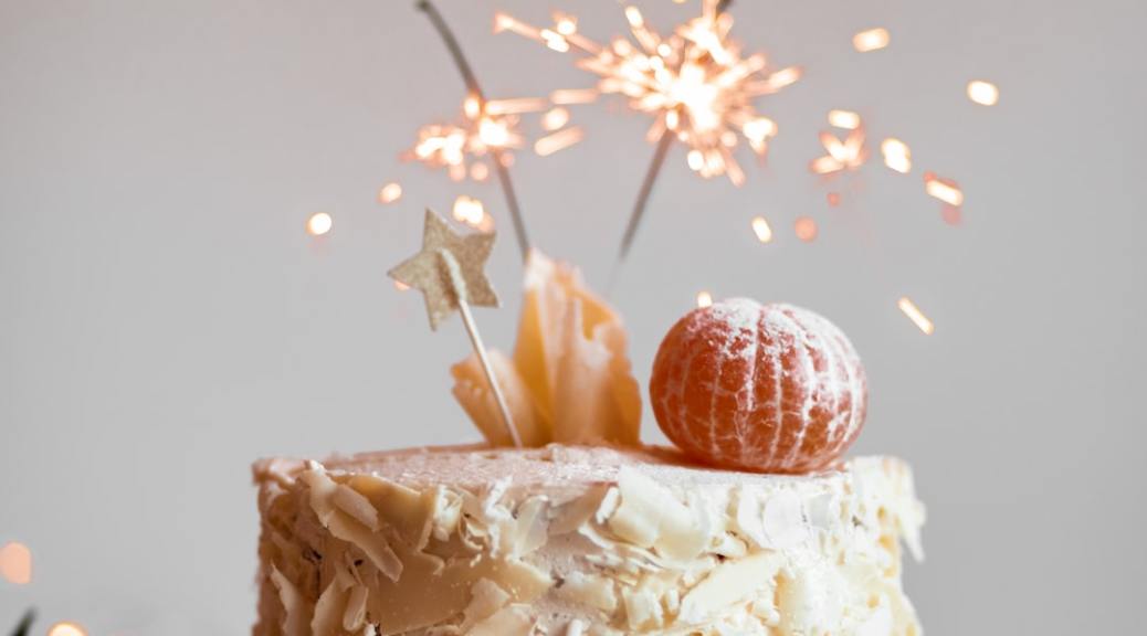 A beige birthday cake with sparklers and oranges on top